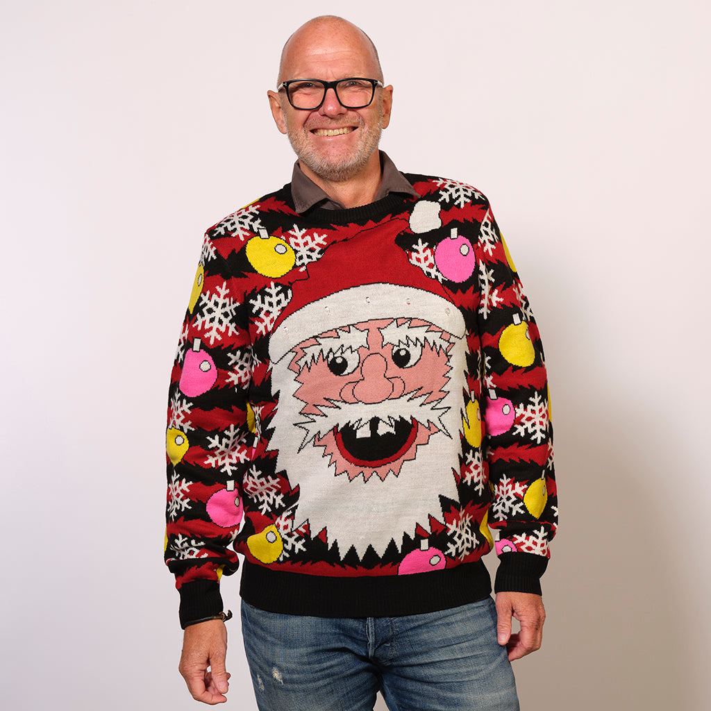 En smilende mand står iført en julesweater med et nissehoved.